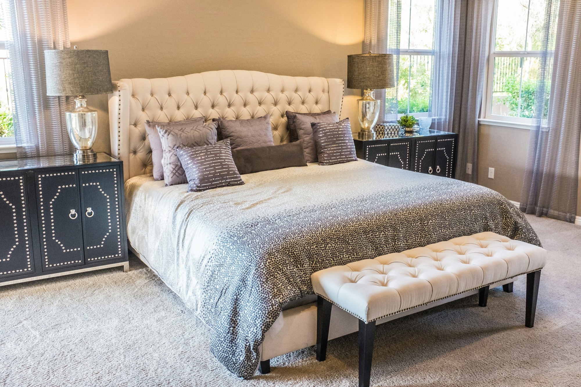 A bright bedroom with a made bed and a tufted bench.